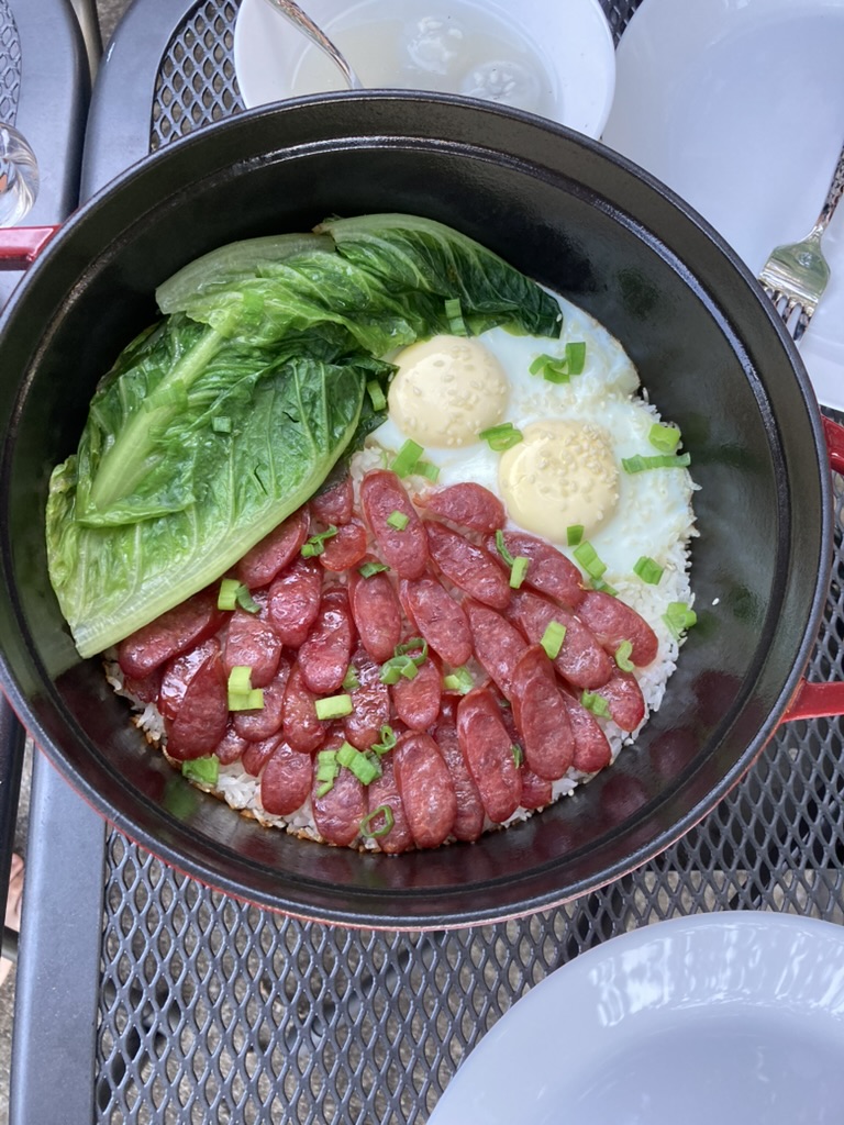 A dutch oven filled with rice, sausage, eggs and leafy greens